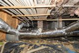 Exposed HVAC ducts and pipes in a crawl space for moisture prevention.