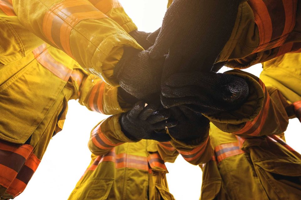 Firefighters in yellow gear unite for fire damage restoration, viewed from below.