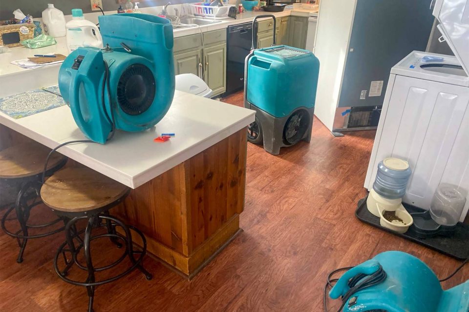 Kitchen with blue dehumidifiers and cleaning tools for water damage restoration.